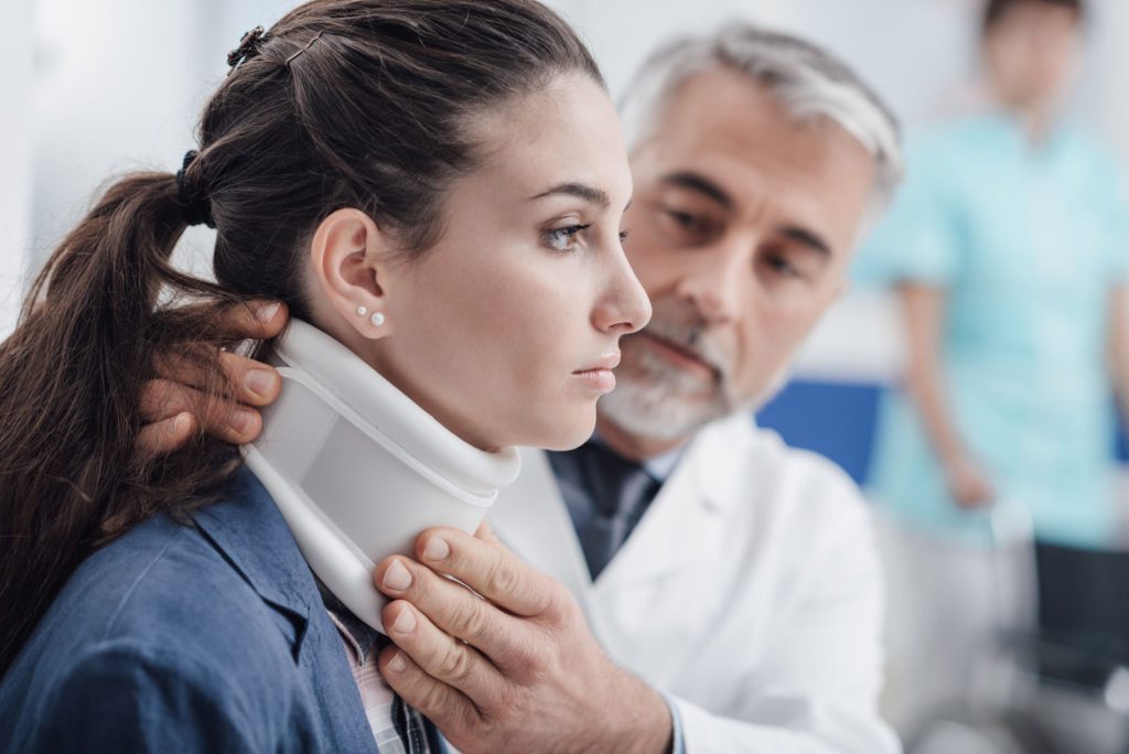 Doctor treating a young injured patient at the ER; he is adjusting her cervical collar.